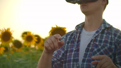 A-student-in-plaid-shirt-and-jeans-uses-VR-glasses-on-the-field-with-sunflowers-for-scientific-article.-These-are-modern-technologies-in-summer-evening.